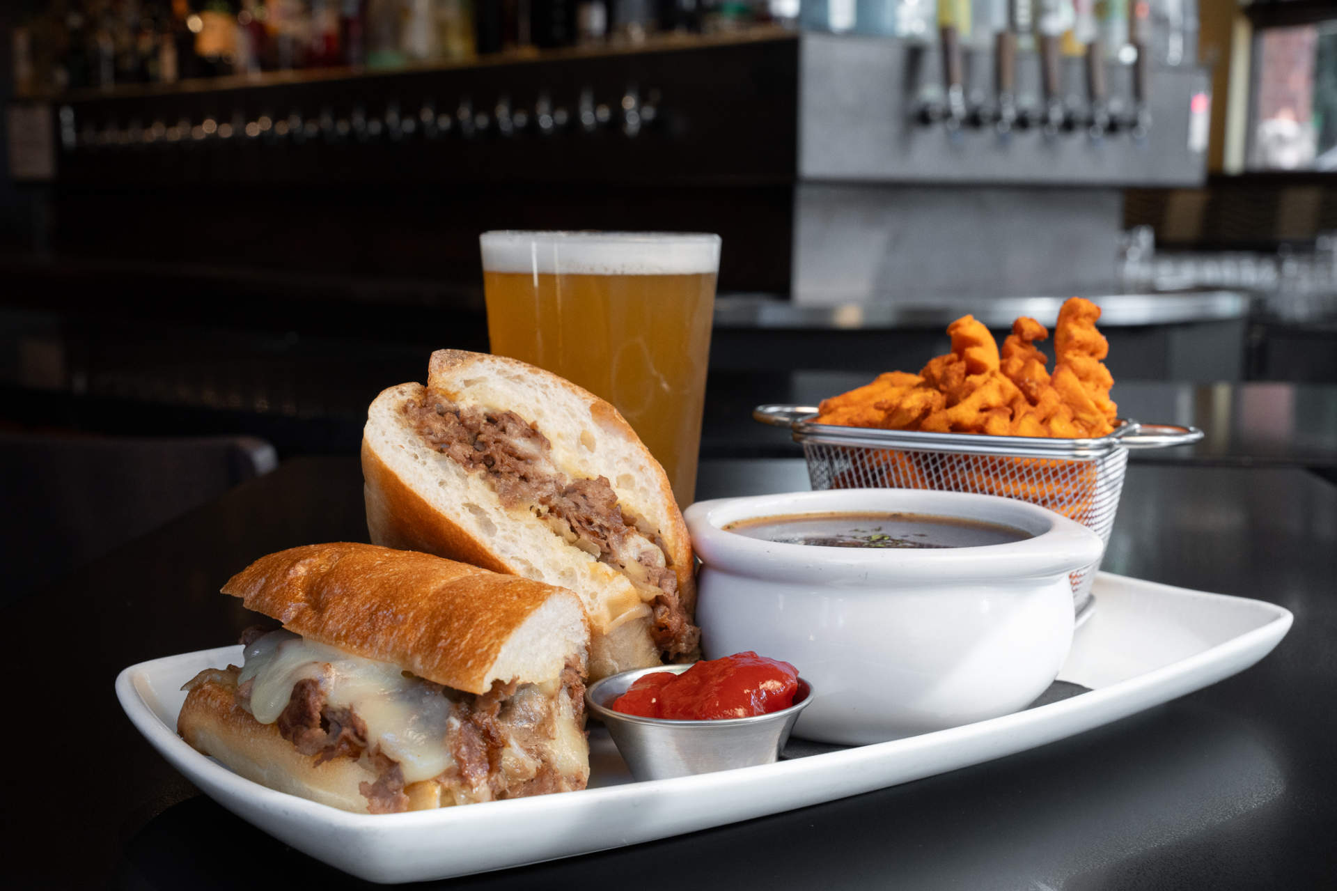 French dip sandwich with au jus, sweet potato fries and a pint of beer