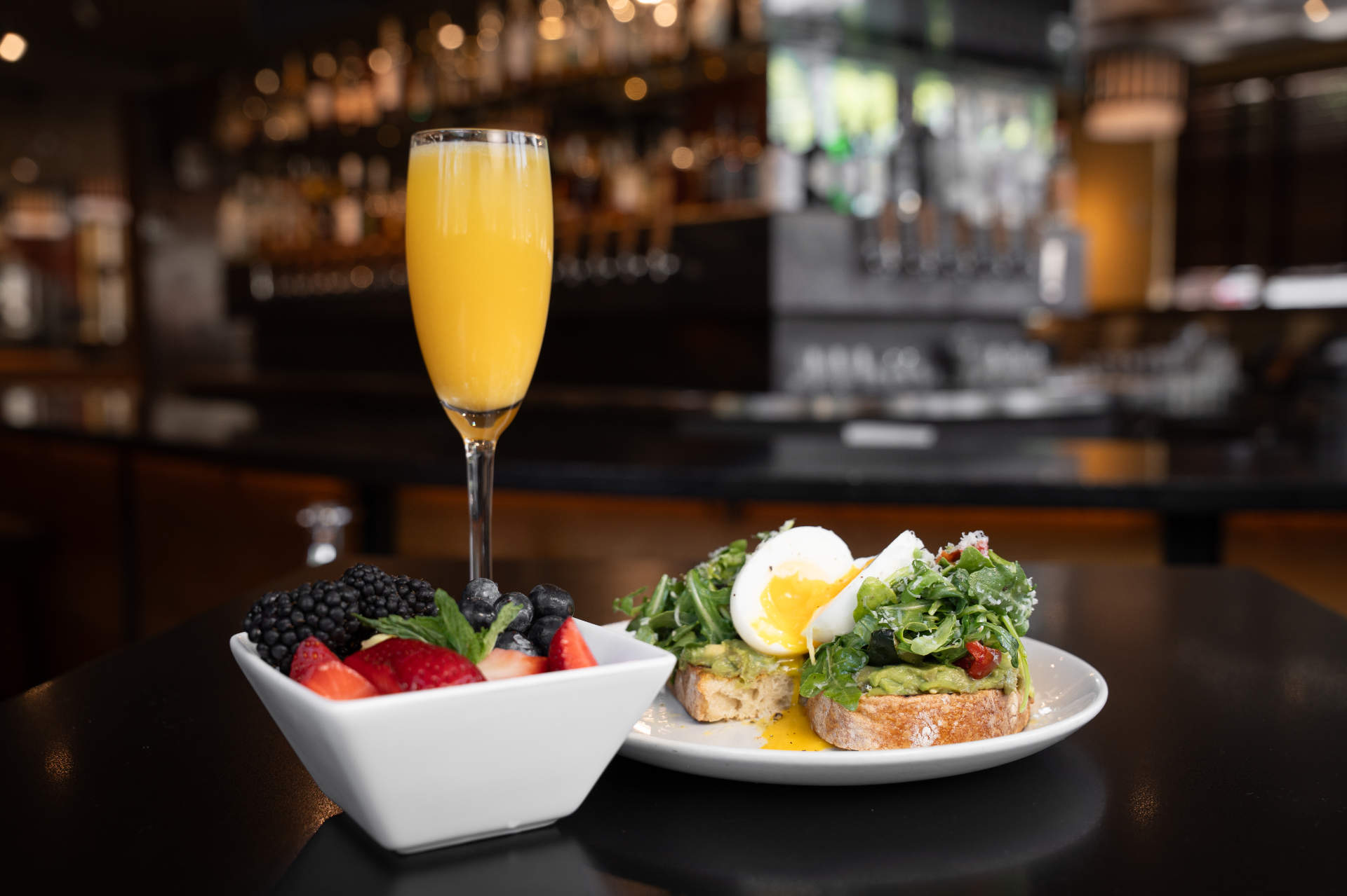 Avocado toast with a soft-boiled egg and arugula, a mimosa and a bowl of fresh berries